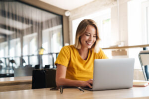 Photo of joyful nice woman using laptop and smiling while sitting.
